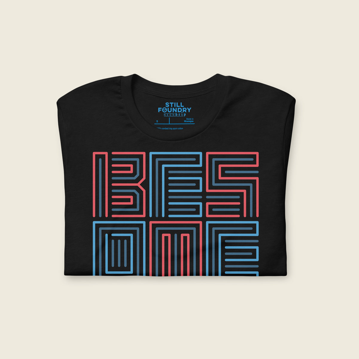 Folded black t-shirt featuring a bold geometric typographic design that reads “BE SOMEONE” in stacked red and blue outlined lettering, with small text below that reads “H-town.”
