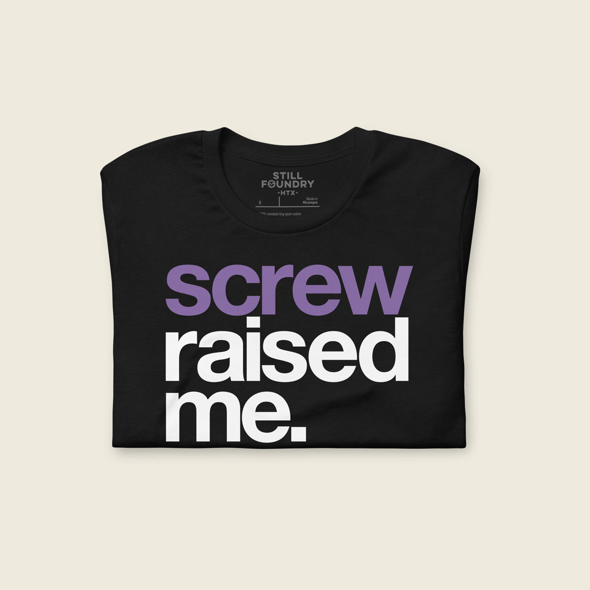 Folded black t-shirt with the phrase “screw raised me.” printed on the front in large bold letters, with “screw” in purple and “raised me.” in white.