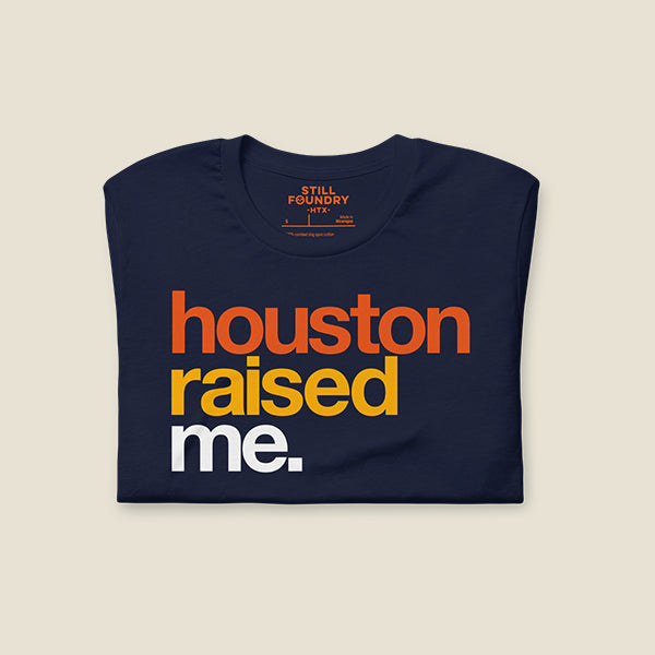 Navy blue t-shirt folded with bold, colorful text on the front that reads "houston" in orange, "raised" in yellow, and "me." in white.