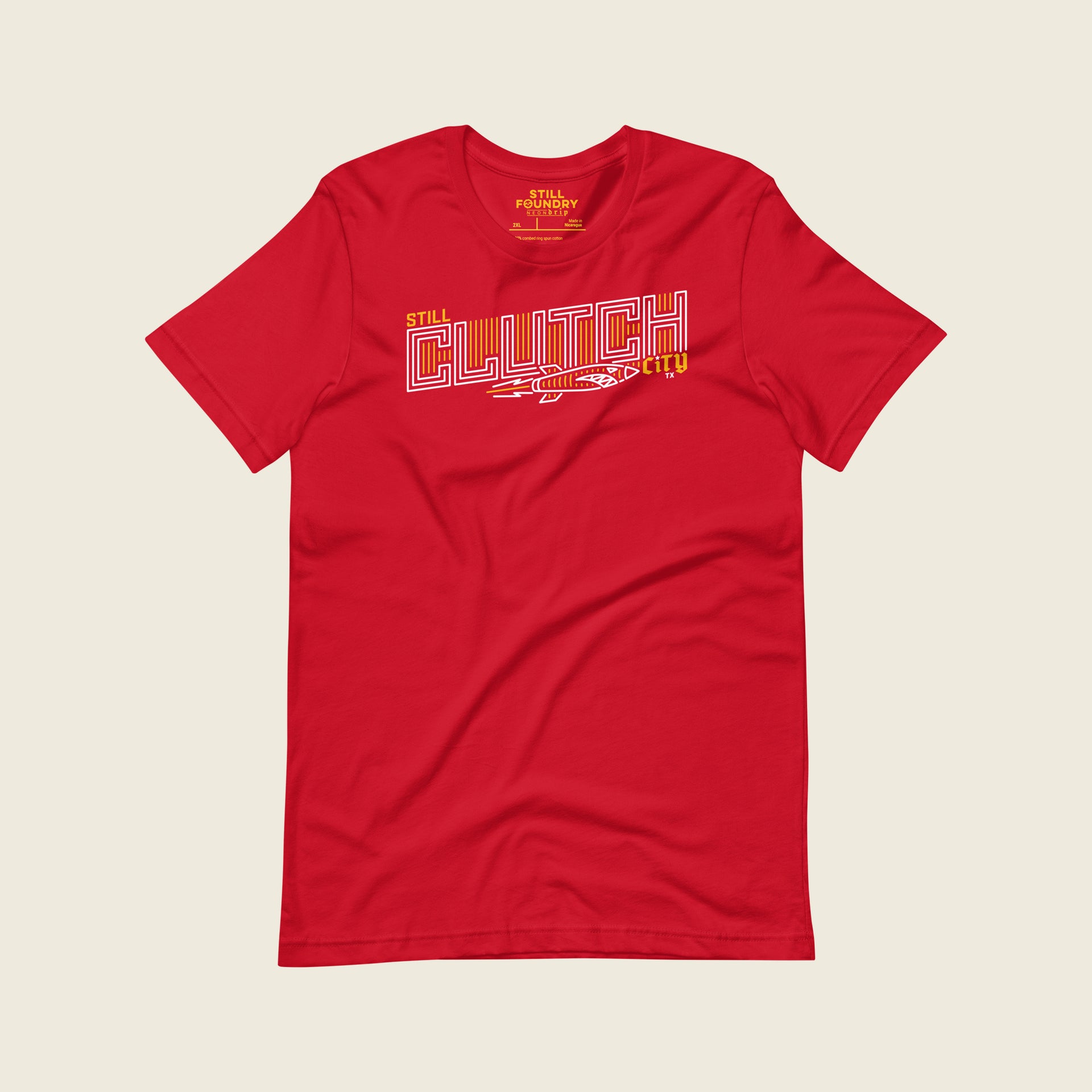 Red t-shirt featuring a bold, outlined graphic that reads “Still Clutch City” in stylized white and yellow lettering, with a dynamic rocket illustration underneath.
