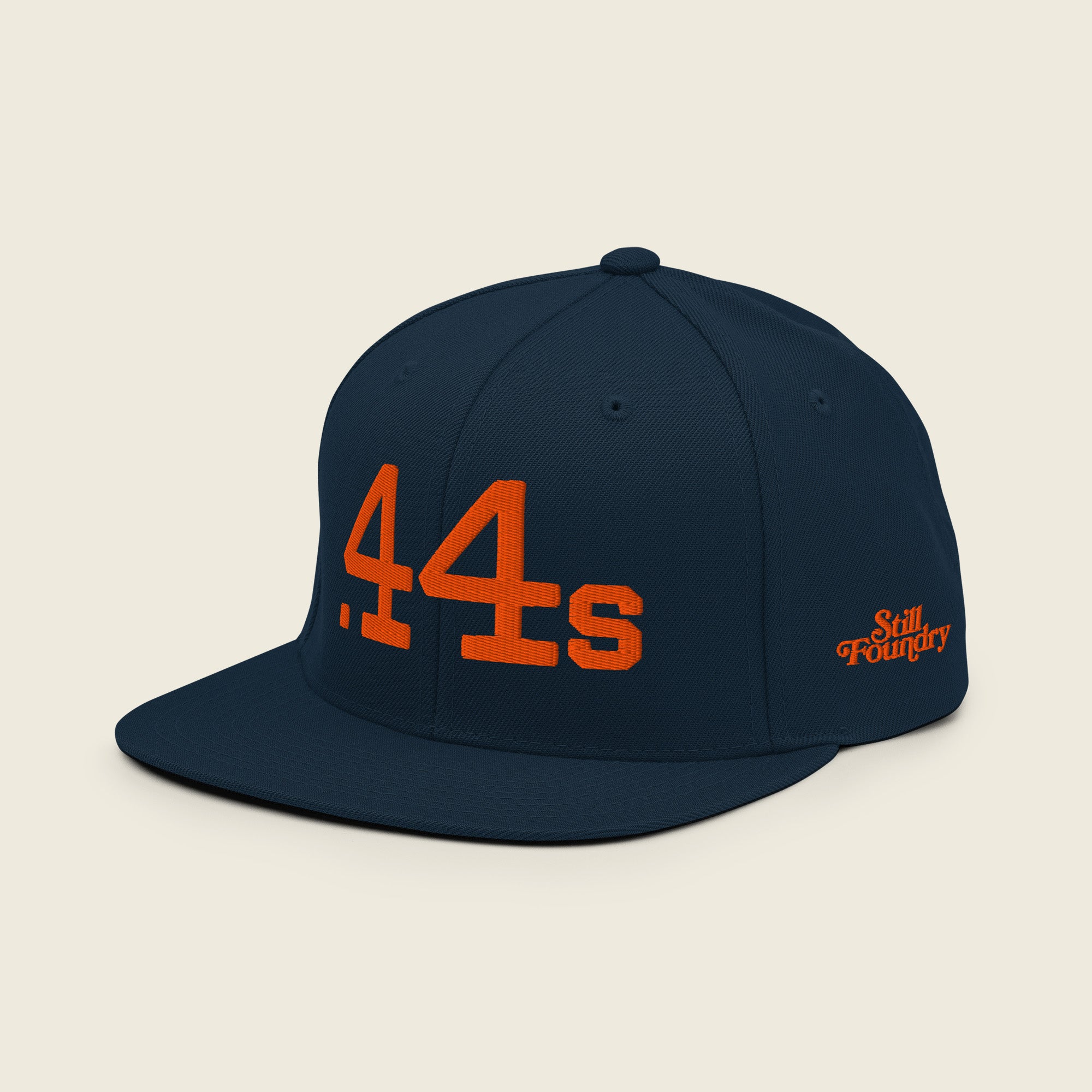 Angled view of Still Tippin .44s navy snapback featuring orange embroidery and Still Foundry side logo.