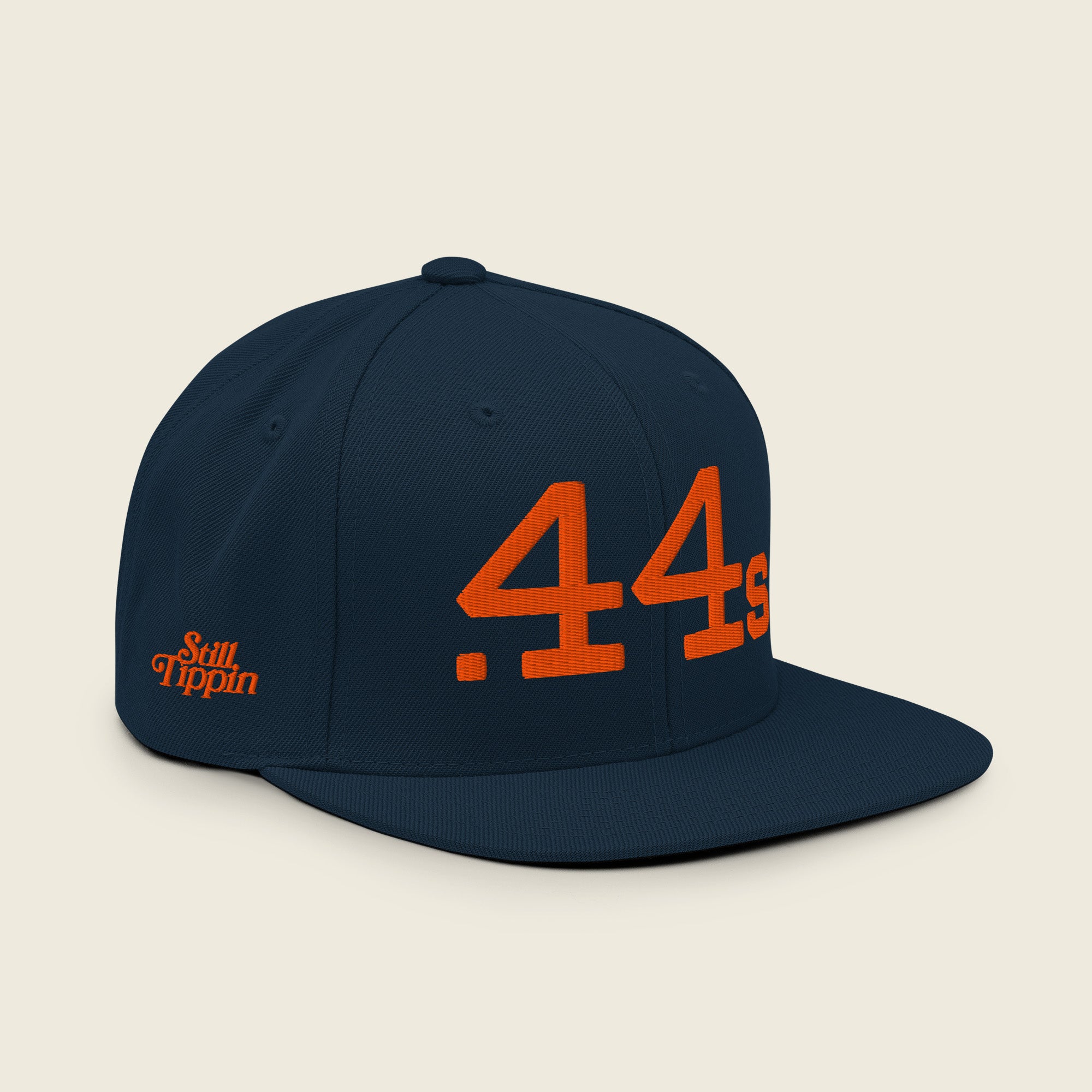 Angled view of Still Tippin .44s navy snapback featuring orange embroidery and Still Tippin side logo.