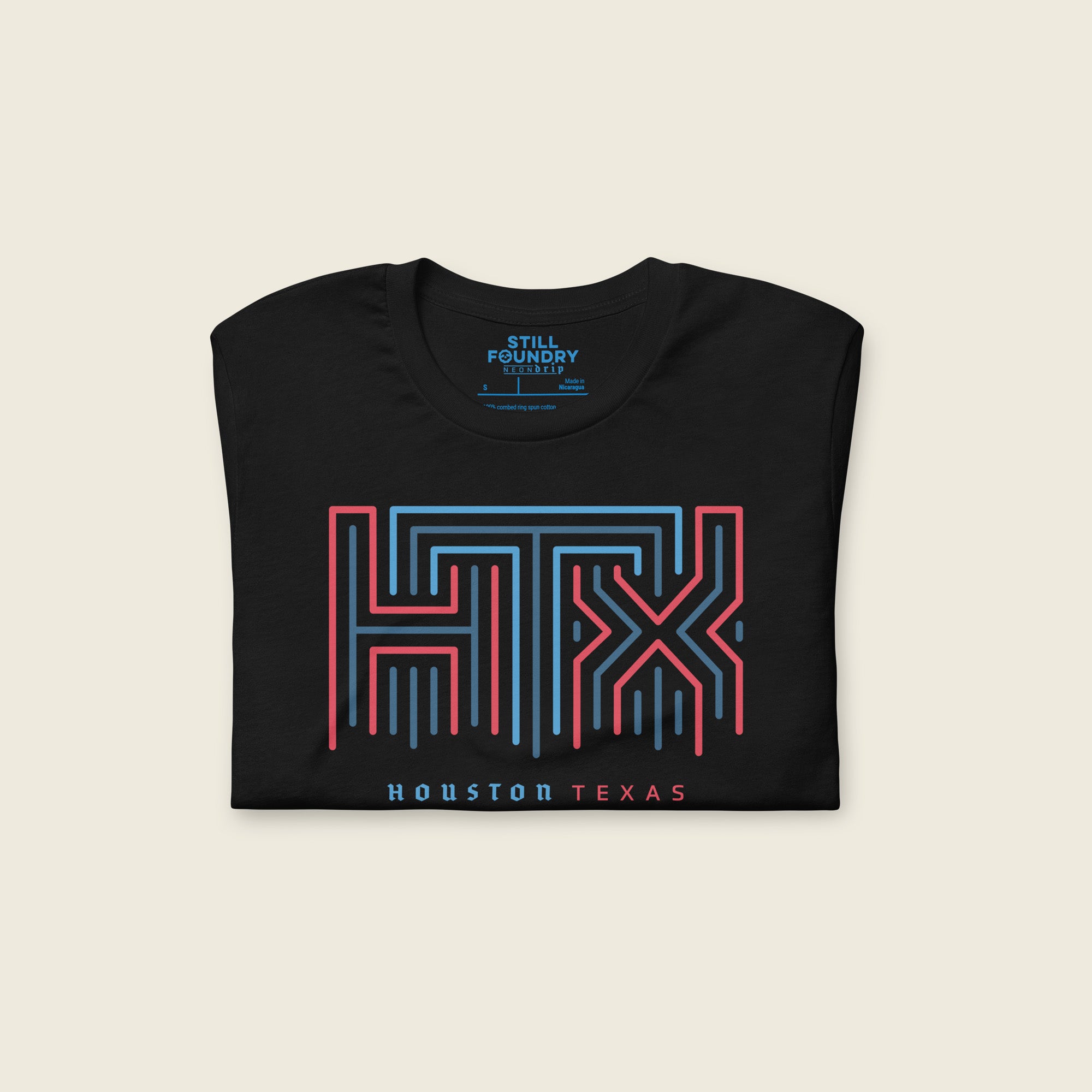 Black short-sleeve t-shirt folded with a large geometric neon sign “HTX” graphic in red and blue on the chest and the words “HOUSTON TEXAS” printed below in small blue and red letters.