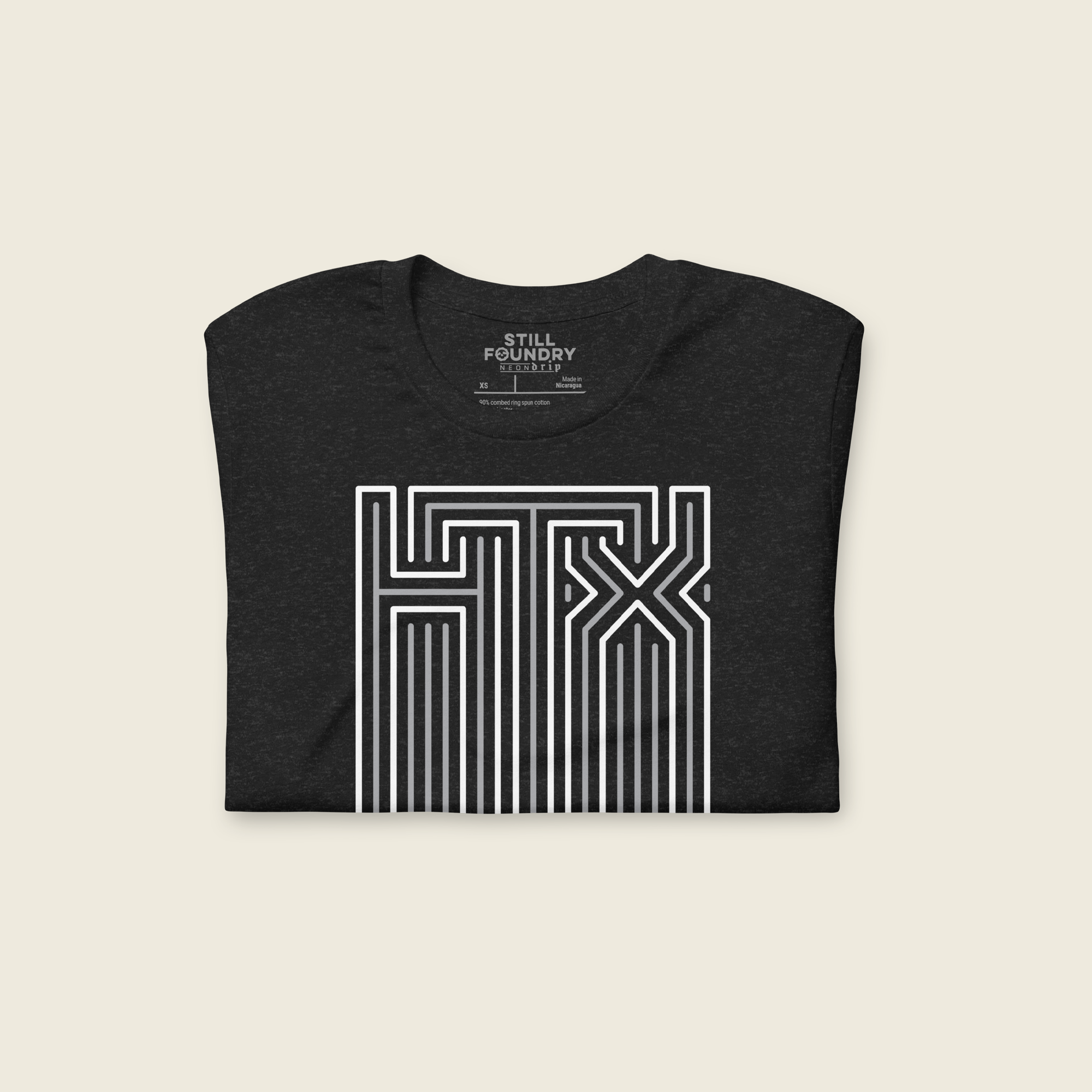 Folded black short-sleeve t-shirt laid flat with a large geometric neon sign “HTX” graphic in white and gray on the chest and the words “HTOWN” printed below in small white old english letters.