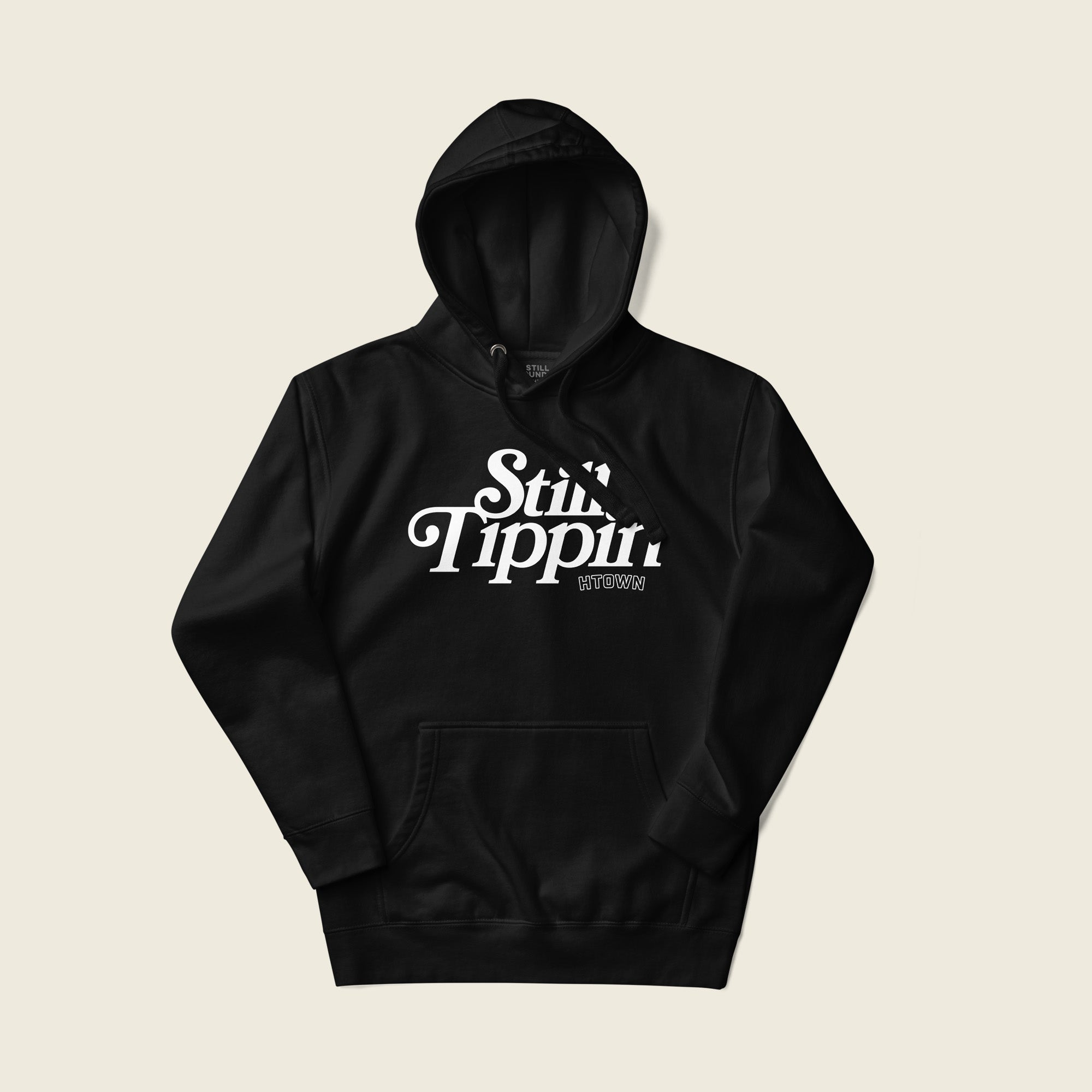 Black hoodie with the phrase "Still Tippin HTOWN" printed in bold white lettering on the front. The text features a stylish, retro font, with "Still Tippin" in large letters and "HTOWN" in smaller block letters underneath. 