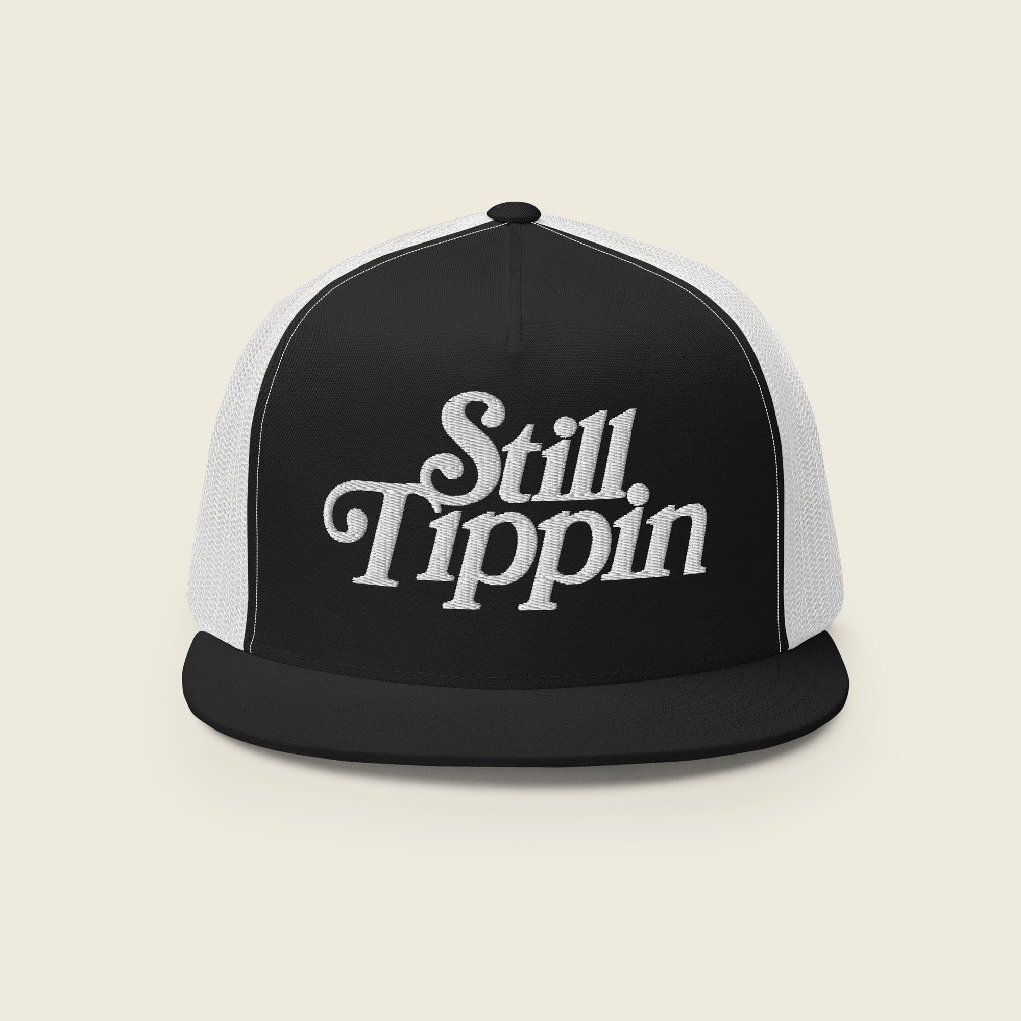 Black and white trucker snapback hat with the phrase "Still Tippin" embroidered in bold white script on the front white panel. The hat features a black bill and black mesh backing.